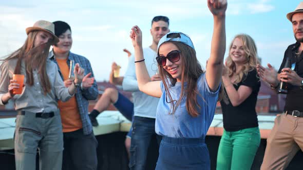 Young Woman Dancing in the Middle of Crowds with Raising Arms at Rooftop Party alt