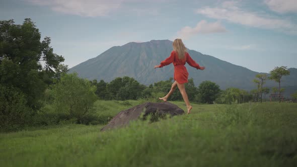Carefree woman running towards boulder and taking in awe-inspiring view of Mount Agung, Savana Tiany alt