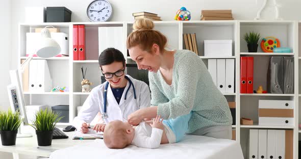 Mom Undressing Child Lying on Table in Doctor Office