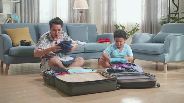Asian Young Dad And Son Packing Clothes In Suitcase At Home, Preparing For Their Vacation alt