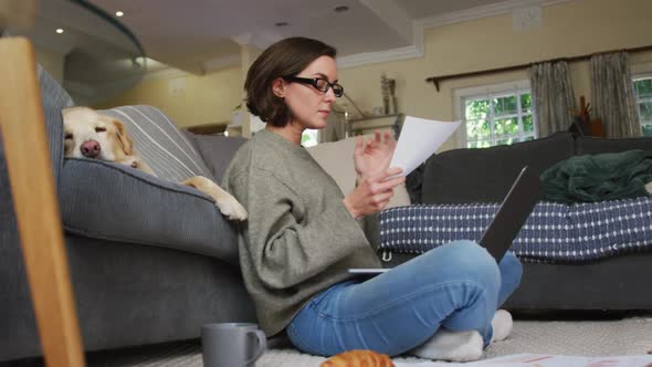 Caucasian woman using laptop working from home with her pet dog on sofa next to her alt