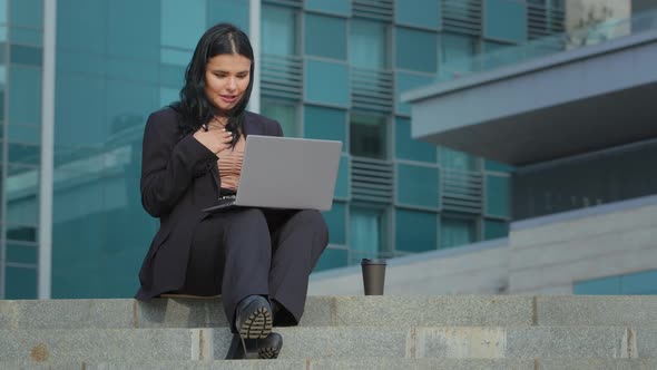 Hispanic Girl Sitting on Steps of Business Center Undergoing Online Interview Using Laptop Presents alt
