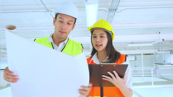 asian Male and Female engineers with helmet walking trough the construction site alt