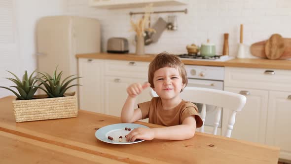 a Little Caucasian Boy Eats Krunchy Breakfast and Enjoys It at Kitchen Table alt