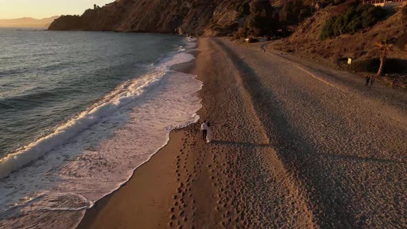 Young couple, newlyweds walking on the beach in Spain sunset