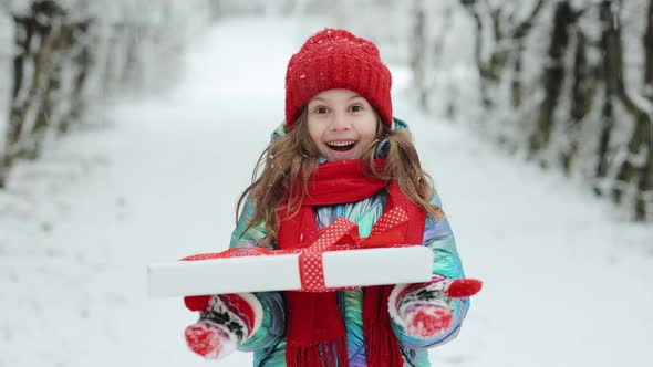 Smiling Girl 6-7 Years Holding in Hands Birthday Present in Festive Package on Winter Background