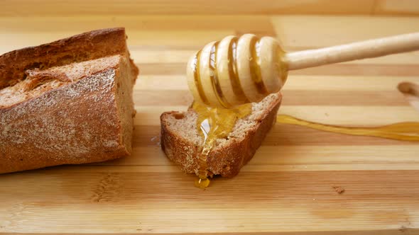 Honey From a Wooden Spoon is Poured Onto a Piece of Brown Bread