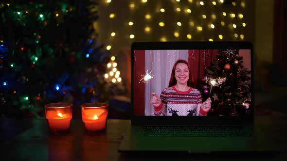 Happy Woman with Sparklers Laughs and Congratulates Relatives on Christmas Via Laptop Online