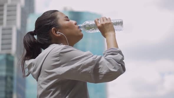 Portrait young Asian woman runner drink water after running and listening to music at a public park.