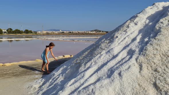 Little redhead girl playing with salt and eat it atSaline of Paceco salt pans Italian nature reserve alt