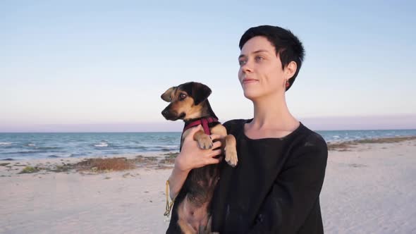 Girl carries her dog, walking along the beach near the sea in slow motion.