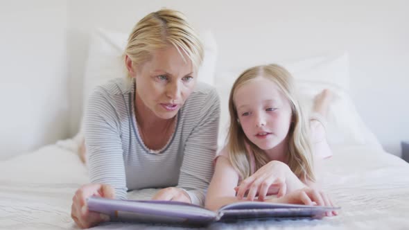 Front view of Caucasian woman reading a story to her daughter on bed alt