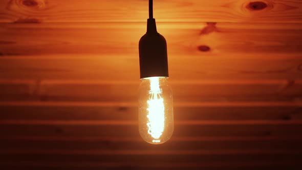 Closeup Shot of Flickering Tungsten Light Bulb Lamp on a Wooden Ceiling