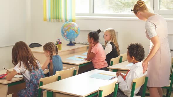 Young Girl Teacher Helps Young Students with a Writing Lesson alt