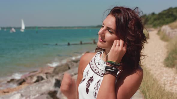 A Young Attract Woman Sat By The Sea Listening To Music On Head Phones alt
