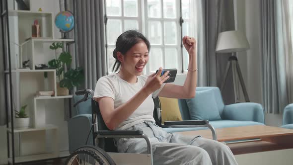 Woman Sitting In A Wheelchair While Use Mobile Phone Playing Video Game And Celebrating At Home alt