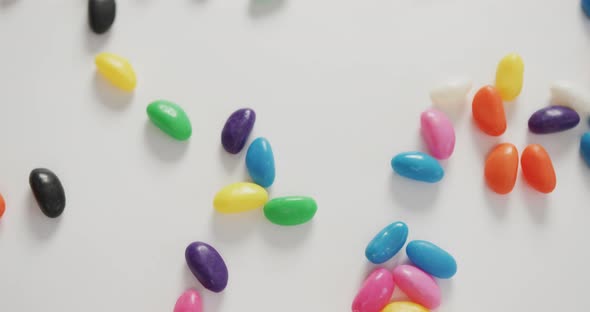 Video of close up of multi coloured sweets spinning over white background alt