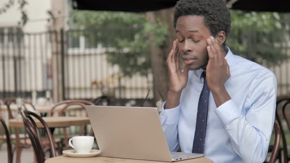 African Businessman with Headache Using Laptop in Outdoor Cafe alt