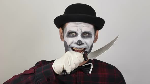 A Horrible Man in Clown Makeup Threatens His Victim with a Sharp Knife. The Scary Clown Looks at the