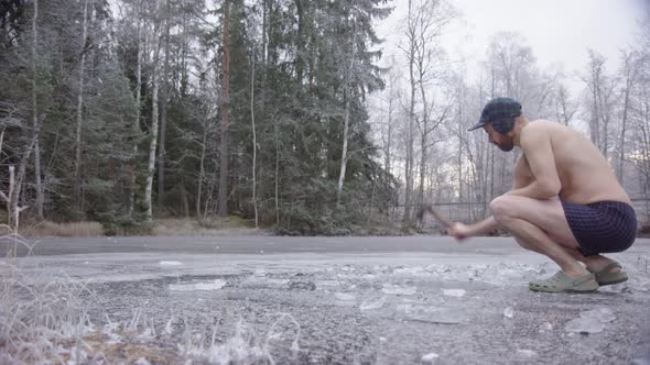 A hipster ice bather enters frame and begins axing the ice to carve a hole alt