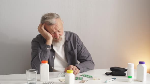 Depressed Senior Man at Home in Kitchen Sitting Behind Desk alt