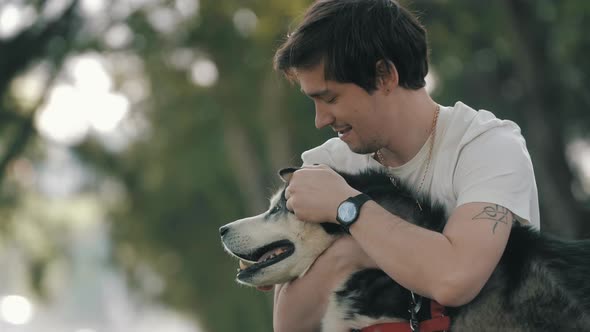 Man caressing Husky dog and sitting on grass in park during stroll.