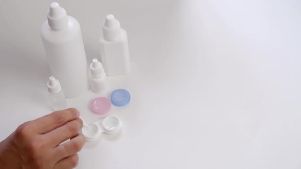 A Woman's Hand Places a Bottle of Lens Cleaning Solution on a White Table alt