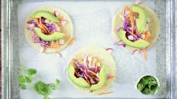Preparing fresh fish tacos with cod and purple cabbage on a white corn tortillas. alt