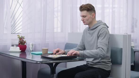 Busy Hurrying Young Male Student Eating Pancakes Drinking Coffee and Leaving Canteen with Tablet alt