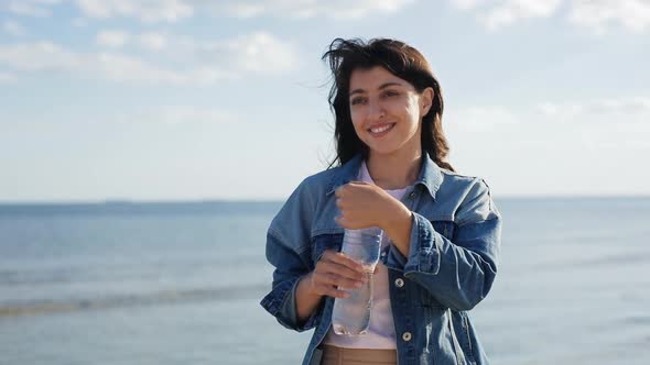 Woman Drinking Clear Mineral Water From Bottle at the Sea. Health Life Concept