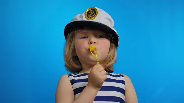 Little Girl in a Sailor Hat is Blowing in a Whistle and in a Studio alt