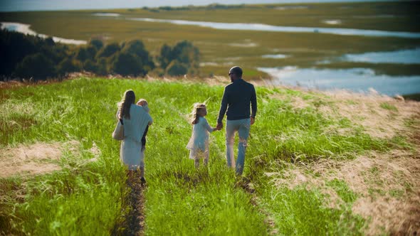 Family of Four Members Walking Down To the Green Field alt