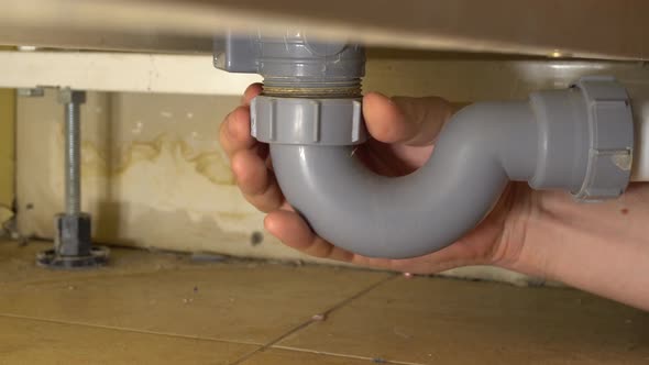 plumber's man's hand unclogs the drain under the tub.