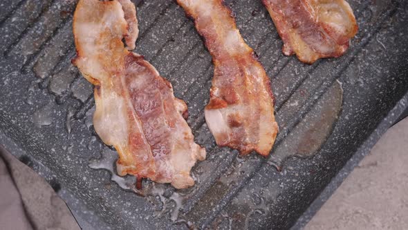 Cooking Pieces of Flavorful Sliced Organic Bacon Fried in Grill Pan alt