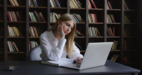 Business Woman in a White Shirt Works at a Laptop and Takes Notes alt
