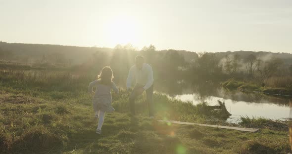 Happy Young Family Is Walking in the Field. A Little Girl Is Running To Her Parents.  alt