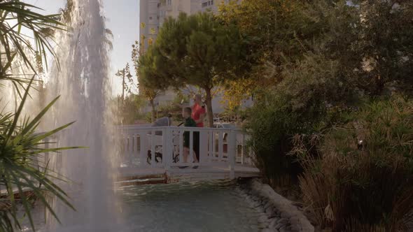 Mother with Children Walking in Hotel Garden with Fountains alt
