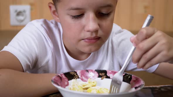 Hungry Teenager Eats Pasta in Home Kitchen and Squints Strongly in Displeasure alt