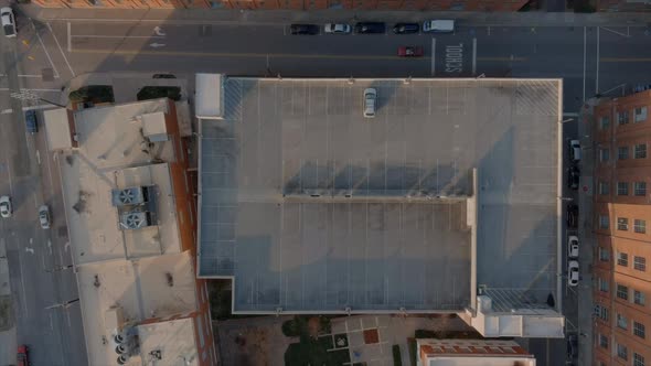 Aerial top-down rising view over building rooftop, parking garage, with parked car in Durham downtow alt