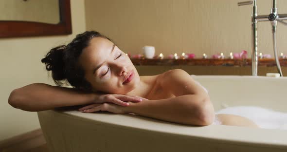 Relaxed biracial woman with vitiligo relaxing in foam bath with candles pampering herself alt