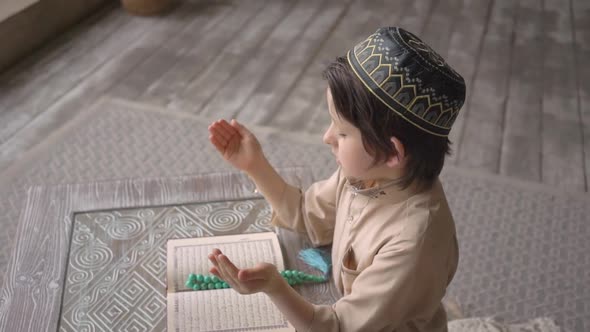 Muslim little boy reading the Koran in prayer hat and arabic clothes with rosary beads
