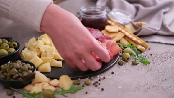 Making Meat and Cheese Antipasto Plater Woman Putting Pieces of Prosciutto Ham on Stone Serving alt