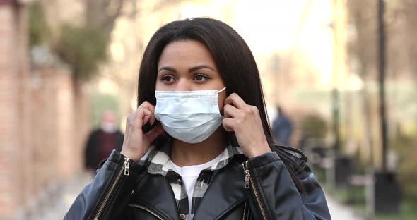 Happy African girl walking outdoor while taking off her protective face mask. alt