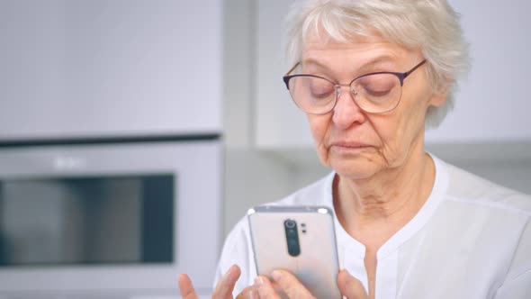 Aged woman manager in glasses and white blouse scrolls social media on smartphone alt