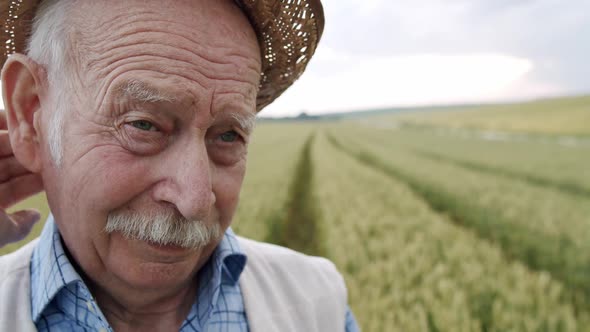 Macro Portrait of Wrinkled Senior Man Looking Thoughtfully and Taking Off Hat alt