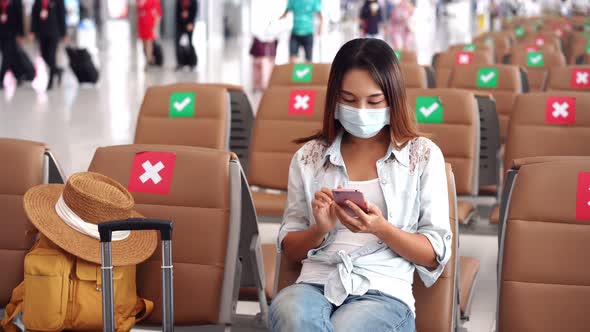 Young woman wearing a surgical mask and using mobile phone at airport alt