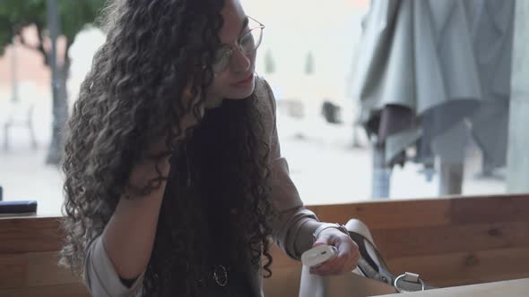 Beautiful Young Woman In Eyeglasses Puts On Bluetooth Earbuds While Sitting Outdoor alt
