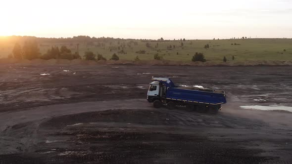 The Drone Flies Around a Powerful Truck with Five Axles of Wheels That is Driving Around the Quarry