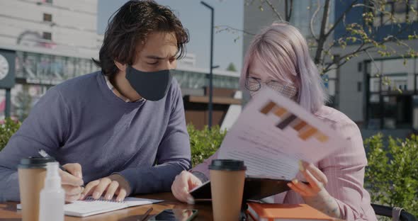 Arab Guy Working Outdoors with Caucasian Colleague Drinking Coffee Wearing Mask During Pandemic alt