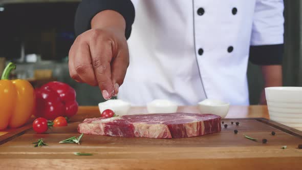 Chef cook season fresh chunk of deli piece of beef with sea salt and grounded spicy peppers.